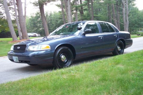 1991 Ford LTD Crown Victoria - This dark blue police sedan is seen from a three-quarter front view, parked on a grassy incline.