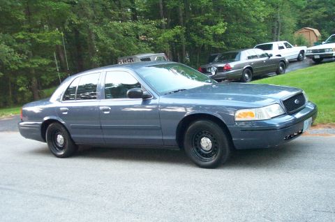 1991 Ford LTD Crown Victoria - A blue Ford Crown Victoria is parked on the side of the road with other vehicles in the background.