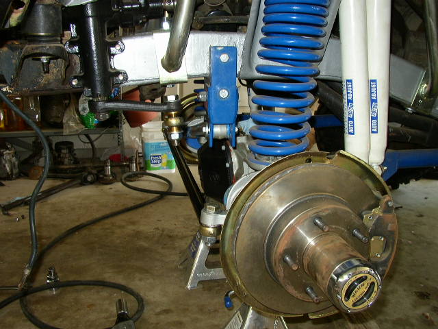 Close-up of a vehicle's front wheel hub, brake rotor, and suspension components, including blue coil springs and white adjustable shocks