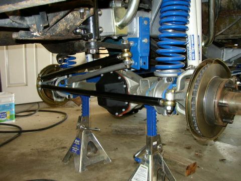 1995 Ford Bronco - Close-up view of a vehicle's modified suspension system, bright blue coilover shocks and disc brakes, supported by jack stands.