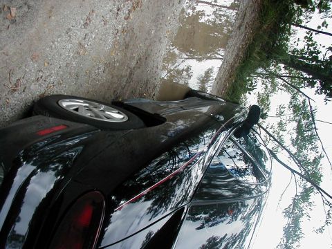 1997 Ford Taurus - A black 1997 Ford Taurus sedan is seen parked on a wet, gravelly road.