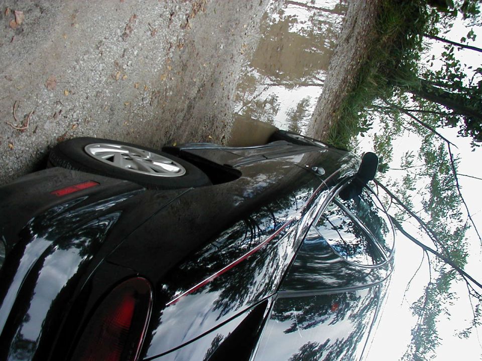 Black 1997 Ford Taurus sedan parked on a gravel road with puddles