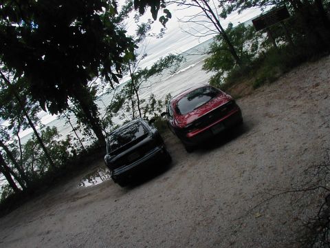 1997 Ford Taurus - Two sedans are parked on a dirt road overlooking a body of water.