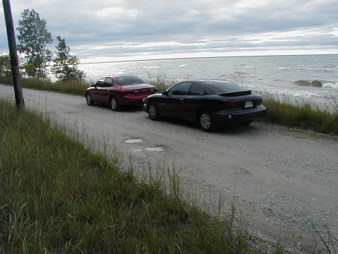 1997 Ford Taurus - Two cars are parked on a dirt road next to a body of water under a cloudy sky. The "SUPERMOTORS" logo is visible in the lower right corner.
