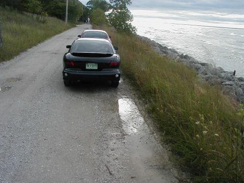 1997 Ford Taurus - Two cars are parked on a gravel road beside a rocky shoreline and a large body of water.