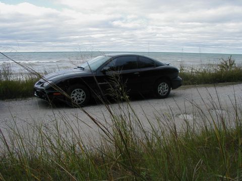 1997 Ford Taurus - A black coupe sits by the water under a cloudy sky, with tall grass obscuring the view.