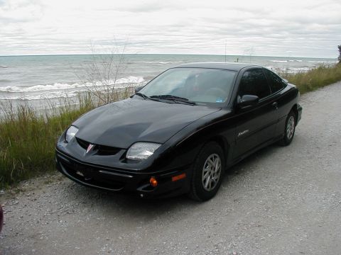 1997 Ford Taurus - A black Pontiac Sunfire coupe is parked on a gravel road next to a body of water.