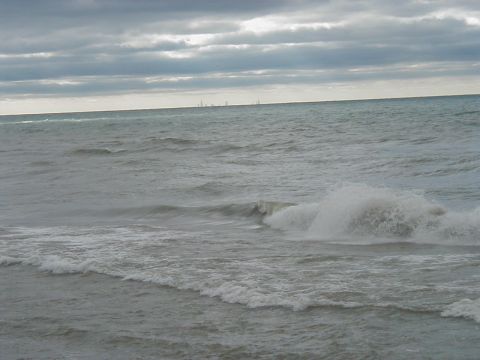 1997 Ford Taurus - Waves break on the shore under a dramatic, cloudy sky, with a faint city skyline visible on the horizon.