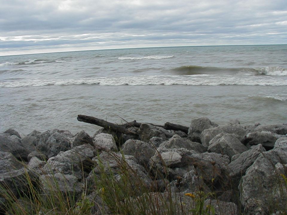 Rocky shoreline with waves under a cloudy sky. Watermark reads SUPERMOTORS