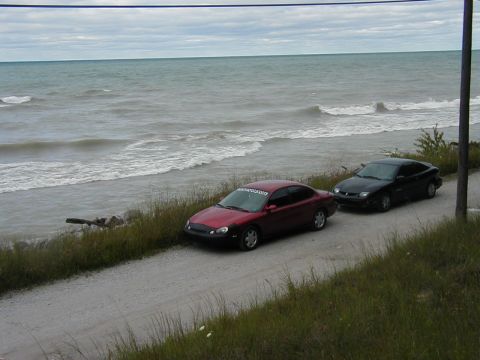 1997 Ford Taurus - Two sedans are parked on a gravel road with waves crashing in the background.