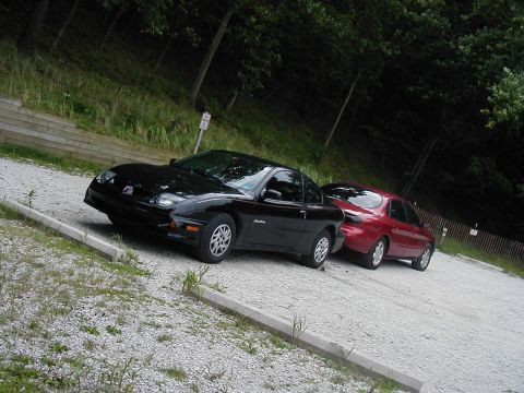 1997 Ford Taurus - Two coupes are parked on a gravel lot next to a wooded area.