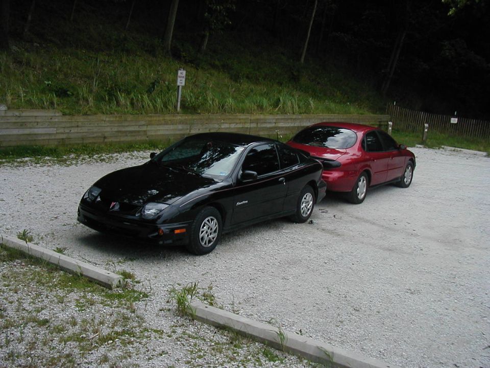 Black coupe and red sedan parked on gravel lot