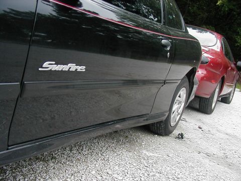 1997 Ford Taurus - Two cars are parked side-by-side on a gravel surface, with trees in the background.