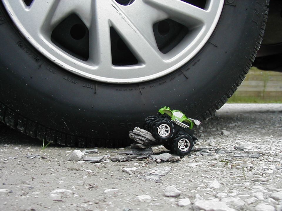 Green toy monster truck on rocks beneath a large tire