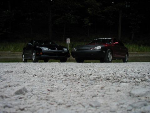 1997 Ford Taurus - A black Pontiac Firebird and a red car with a cover are parked on a gravel lot.