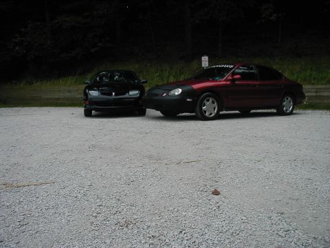 1997 Ford Taurus - Two sedans are parked side-by-side on a gravel lot, with trees in the background.