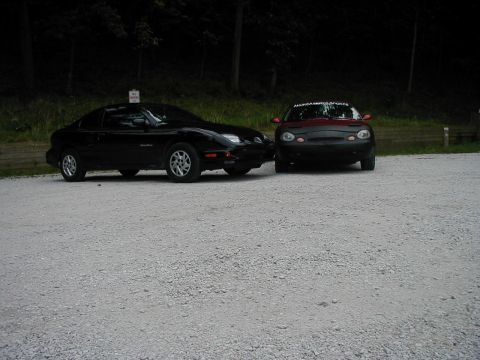 1997 Ford Taurus - Two cars are parked on a gravel lot, with trees visible behind them.