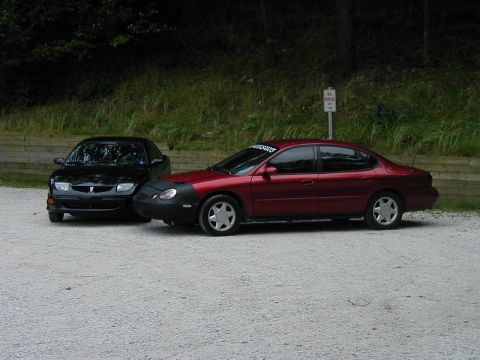 1997 Ford Taurus - Two sedans are parked side-by-side on a gravel lot with trees in the background.