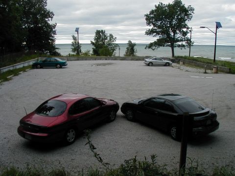 1997 Ford Taurus - Two coupes are parked in a gravel lot with a body of water in the background.