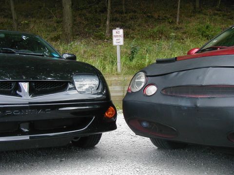 1997 Ford Taurus - Two cars are parked next to each other, one is a black Pontiac and the other is covered.
