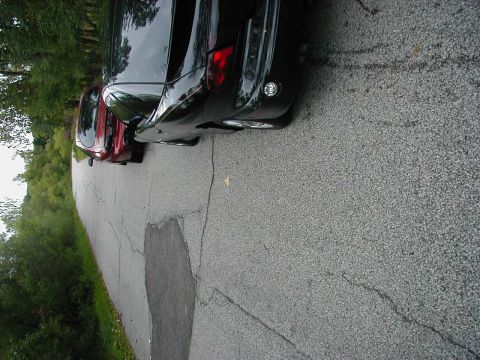 1997 Ford Taurus - Two cars are parked on the side of a road with trees lining the area.