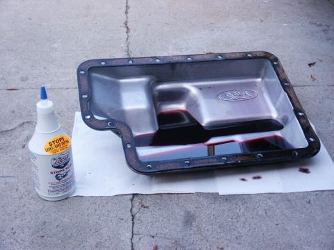 1996 Ford Bronco - A transmission pan, likely from a Ford vehicle, sits on paper with a bottle of stop leak beside it.