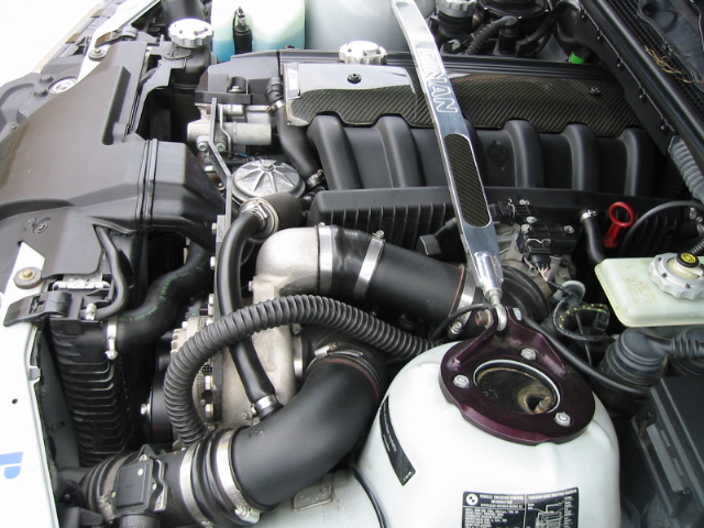 BMW inline-six engine bay with supercharger, black intake piping and carbon-look cover