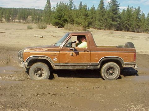 1989 Ford Bronco - A brown Ford Bronco navigates through a muddy terrain with two occupants inside.