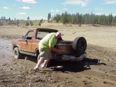 1989 Ford Bronco - A man pushes a brown 1989 Ford Bronco that is stuck in the mud.