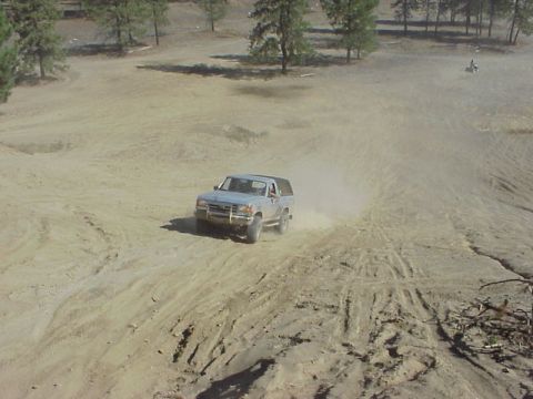 1989 Ford Bronco - A 1989 Ford Bronco navigates a dusty, off-road terrain, leaving tracks behind.