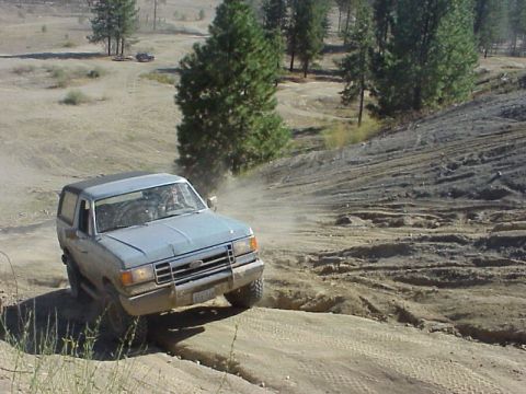 1989 Ford Bronco - A Ford Bronco navigates a dusty off-road trail, with another vehicle in the distance.