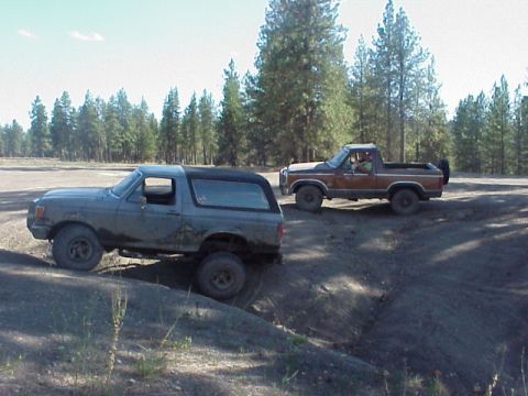1989 Ford Bronco - A gray 1989 Ford Bronco navigates an off-road trail, followed by a brown pickup truck.
