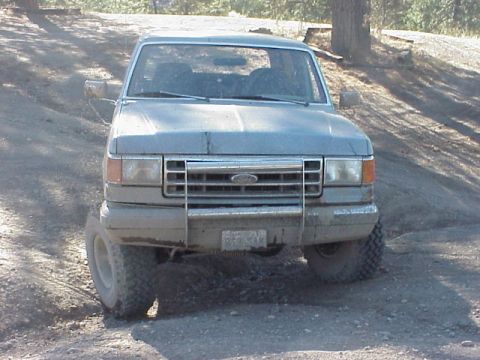 1989 Ford Bronco - A dusty gray Ford Bronco is parked on a dirt road, facing the camera.