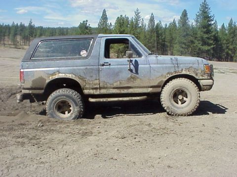 1989 Ford Bronco - A blue Ford Bronco is stuck in the mud with trees in the background.