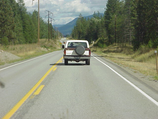 Brown and white Ford Bronco with spare tire on rear, driving on a highway