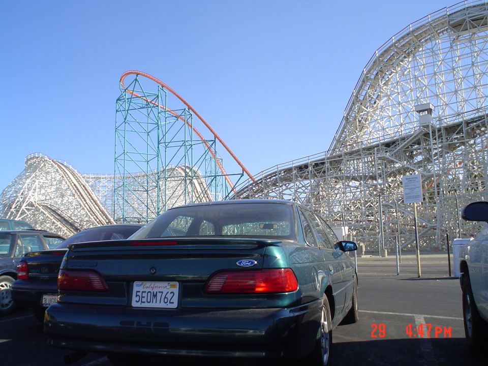 Green Ford SHO sedan rear parked before wooden and steel roller coasters