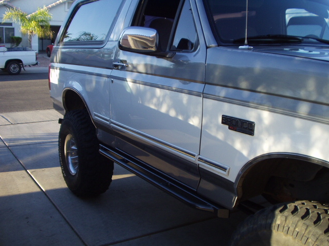 Side view of a lifted white and gray Ford Bronco XLT on mud tires in a residential driveway