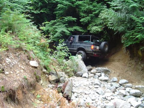 1993 Ford Bronco - A 1993 Ford Bronco navigates a challenging, rocky path through a dense forest.