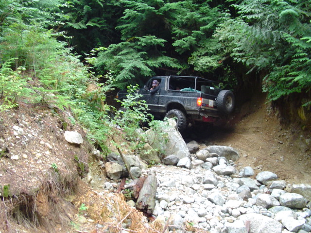 Black 1993 Ford Bronco driving on a rocky, wooded trail