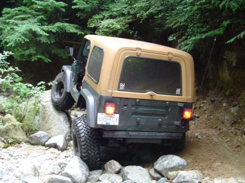 1993 Ford Bronco - A tan hardtop Jeep Wrangler TJ navigates a rocky trail, demonstrating its off-road capability.