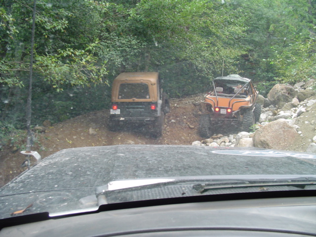Two off-road vehicles driving on a dirt path with trees and rocks around