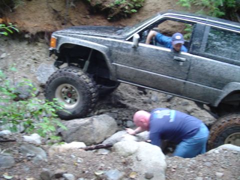 1993 Ford Bronco - An off-road vehicle struggles on a steep, rocky terrain with assistance from a person on the ground.