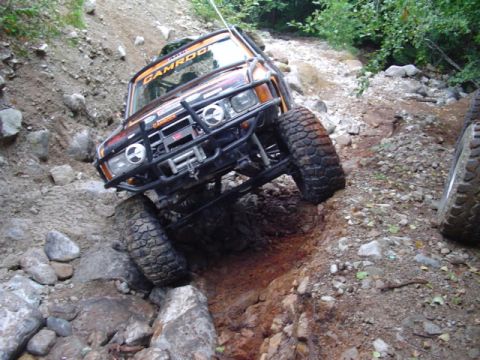 1993 Ford Bronco - This heavily modified off-road vehicle navigates a challenging rocky trail, with another vehicle visible to the right.