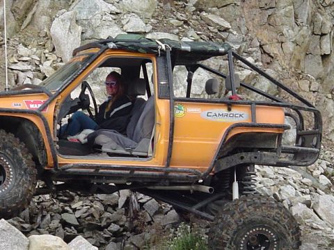 1993 Ford Bronco - An orange off-road vehicle navigates rocky terrain, a prominent roll cage and custom modifications.
