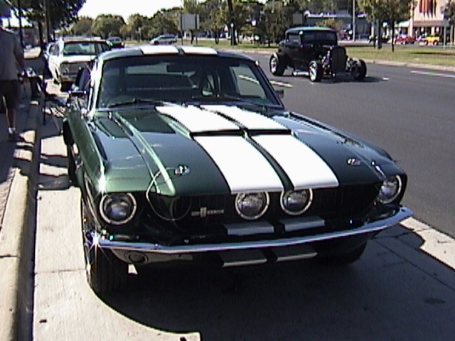 Dark green classic Mustang fastback with white racing stripes, front view parked at a curb