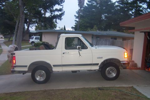 1990 Ford Bronco - A white 1990 Ford Bronco is parked in front of a garage, viewed from the side.