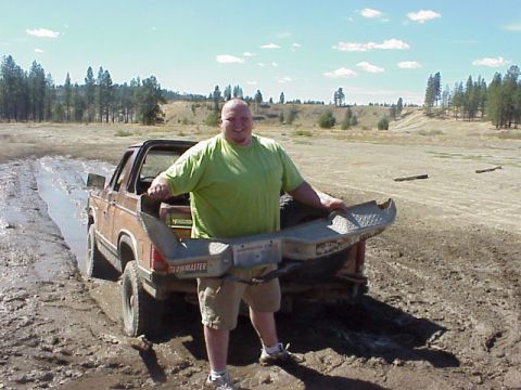 1989 Ford Bronco - Man holds a bumper in front of a muddy 1989 Ford Bronco.