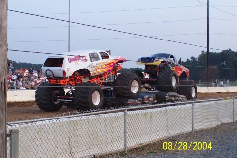 1979 Ford Bronco II - Monster trucks perform at an event, crushing vehicles beneath their massive tires.