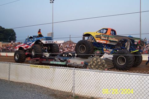 1979 Ford Bronco II - Monster trucks 'Bigfoot' and 'Black Stallion' perform a car crush demonstration for a crowd.