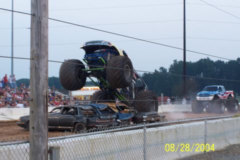 1979 Ford Bronco II - A monster truck soars over a pile of demolished cars during an event, with another monster truck visible in the distance.